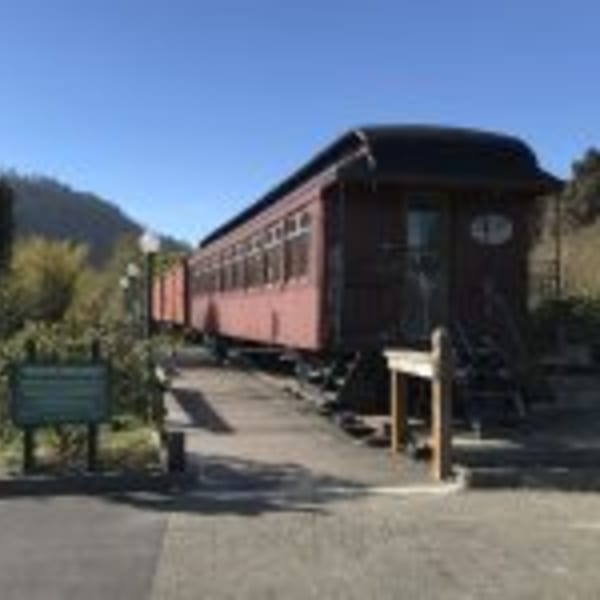 A red train car, part of the Cape Fear Café, sits on tracks next to a paved path.