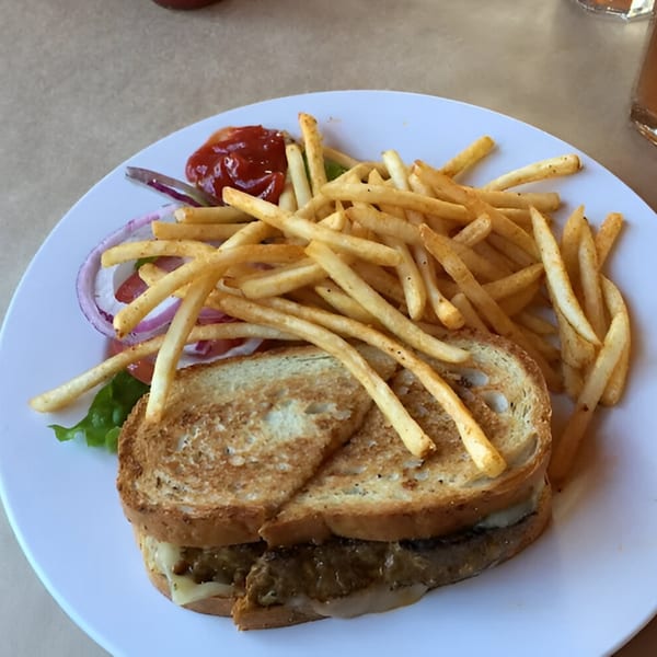 Grilled sandwich with melted cheese and meat, served with a side of french fries, lettuce, and red onion.