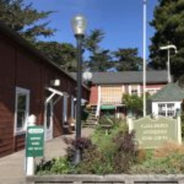Exterior view of Cape Fear Café, a red building with green signs and lush landscaping under a blue sky.