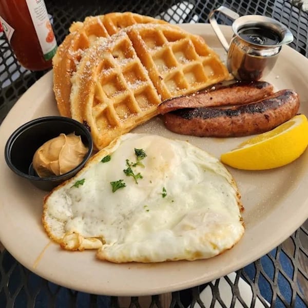 Breakfast plate with waffles, sausages, fried eggs, peanut butter, and a lemon wedge.