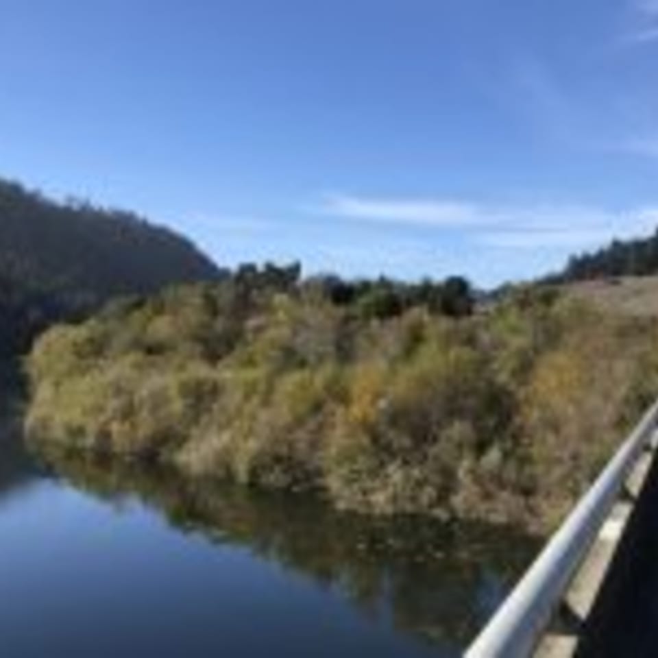 A scenic view of a calm body of water reflecting green and brown hills under a clear blue sky.